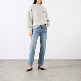 Model wearing Anine Bing grey cotton sweat top with small chest graphic, styled with light blue straight-leg jeans and black mules.