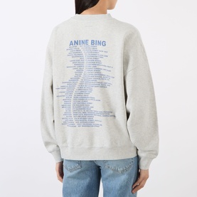 Model wearing Anine Bing grey cotton sweat top, back view showing blue graphic text print, styled with light blue jeans.