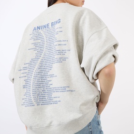 Model wearing Anine Bing grey cotton sweat top, back view showing blue branded graphic text print across the back.