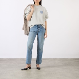 Model wearing Anine Bing grey cotton sweat top with blue straight-leg jeans and black kitten heel mules, holding a beige jacket