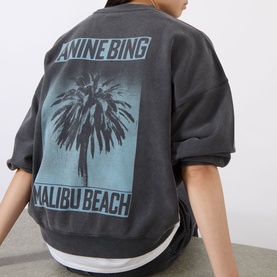 Model wearing Anine Bing black cotton sweat top, back view showing Malibu Beach palm tree graphic print in blue-grey.