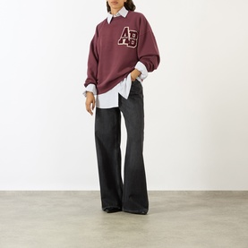 Model wearing Anine Bing burgundy cotton sweat top with AB logo patch, styled with white shirt and black wide-leg jeans.