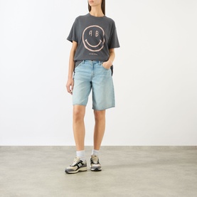 Model wearing Anine Bing washed grey graphic T-shirt with smiley face print, styled with light blue denim shorts and trainers