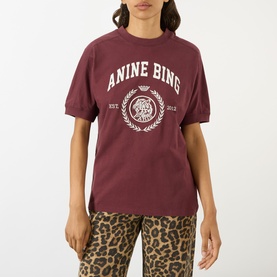 Model wearing Anine Bing burgundy cotton T-shirt with white collegiate logo print, styled with leopard-print trousers.