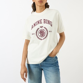 Model wearing Anine Bing ecru cotton T-shirt with burgundy collegiate logo graphic, styled with blue jeans.