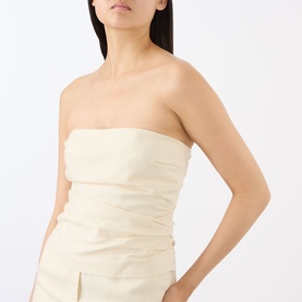 Model wearing Anine Bing cream strapless ruched tube top with coordinating cream skirt with front split visible below.