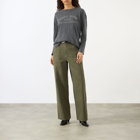 Model wearing Anine Bing Ivan Paris Stencil Top in black, long sleeves, logo graphic front, styled with wide-leg khaki trousers and black heels.