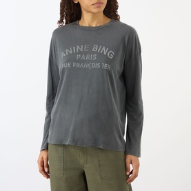 Model wearing Anine Bing Ivan Paris Stencil Top in black, long-sleeve cotton tee with logo graphic, styled with khaki trousers.