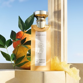 Bulgari Eau Parfum&eacute;e au Th&eacute; Imp&eacute;rial EDT in tall gold-capped bottle, styled with citrus fruits and green leaves against a sunlit column backdrop.