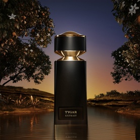 Bulgari Tygar Extrait de Parfum in black bottle with gold cap, set against a warm dusk landscape with trees and water reflection.