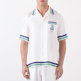 Model wearing Casablanca Hotel Emblem Silk Shirt in white with navy and green stripe trims, camp collar, short sleeves, and chest patch pocket.