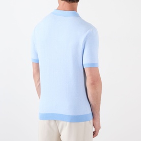 Model wearing Casablanca Pinstripe Logo Polo Shirt in light blue, rear view showing ribbed trims and knit structure, styled with cream trousers.