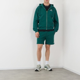 Model wearing Casablanca Sport green zip-up hoodie and matching shorts, styled with white socks and grey trainers.