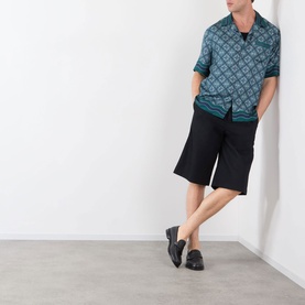Model wearing Casablanca Radiating Monogram Silk Shirt in teal, styled with black shorts and black loafers.