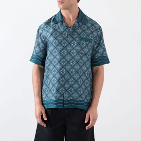 Model wearing Casablanca Radiating Monogram Silk Shirt in teal, featuring camp collar, short sleeves, monogram print and wavy stripe trim detail.