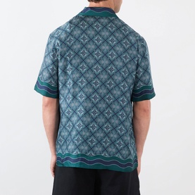 Model wearing Casablanca Radiating Monogram Silk Shirt, rear view, teal diamond monogram print with wavy stripe hem trim, short sleeves