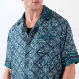Model wearing Casablanca Radiating Monogram Silk Shirt in teal geometric print, camp collar, short sleeves, with chest patch pocket visible
