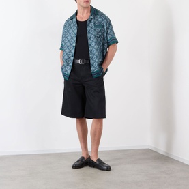 Model wearing Casablanca Radiating Monogram Silk Shirt in teal, styled with black shorts, belt and loafers