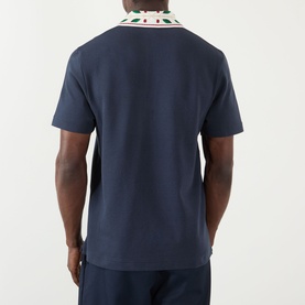 Model wearing Casablanca Laurel Piqu&eacute; Polo Shirt in navy, rear view showing laurel-embroidered collar and short sleeves. Styled with navy trousers.