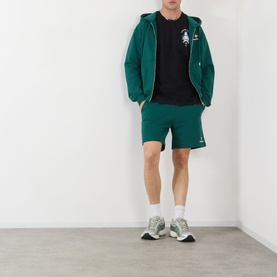Model wearing Casablanca Logo Sweat Shorts in green with matching zip hoodie, black graphic tee, white socks and grey trainers.