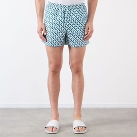 Model wearing Casablanca Monogram Motif Swim Shorts in Cubist CC Monogram print, styled with white slider sandals.