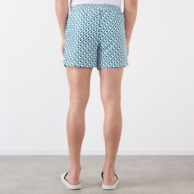 Model wearing Casablanca Monogram Motif Swim Shorts in Cubist CC Monogram print, teal and white geometric pattern, back view, styled with slip-on