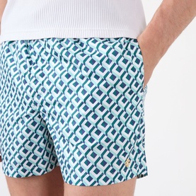 Model wearing Casablanca Monogram Motif Swim Shorts in Cubist CC Monogram print, teal and white geometric pattern, with white top.