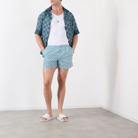 Model wearing Casablanca Monogram Motif Swim Shorts in Cubist CC Monogram print, styled with matching shirt and white slides.