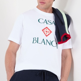 Model wearing Casablanca Diamond Logo T-Shirt in white with stacked logo graphic print, styled with navy joggers and a striped jacket over shoulder.