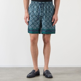 Model wearing Casablanca Radiating Monogram silk shorts in teal geometric print with elasticated waist, styled with navy loafers.