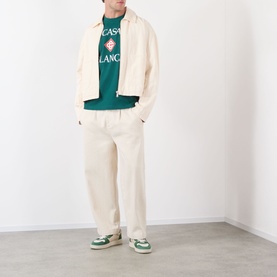 Model wearing Casablanca Diamond Logo T-Shirt in green with graphic print, styled with cream jacket, wide-leg trousers and green trainers.