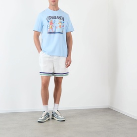 Model wearing Casablanca Egyptian Tennis Match Logo T-Shirt in light blue with white shorts and grey trainers.