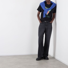Model wearing Casablanca Tennis Club Icon Pyramid Abduction T-Shirt in black with blue hoodie draped over shoulders, styled with dark grey jeans and