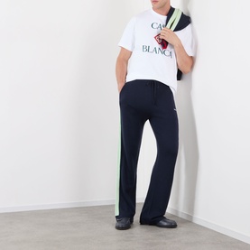 Model wearing Casablanca Logo Merino Wool Track Pants in navy with green side stripe, styled with a white Casablanca logo tee and black shoes.