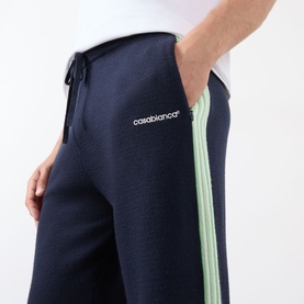 Model wearing Casablanca Logo Merino Wool Track Pants in navy with mint green contrast side stripes and drawstring waistband.