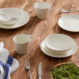 Royal Doulton white dinnerware set styled on a wooden table, including plates, bowls and mugs with cutlery and folded napkin