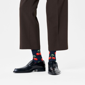 Model wearing Happy Socks navy and red cherry-print socks, styled with dark brown cropped trousers and black patent leather shoes.