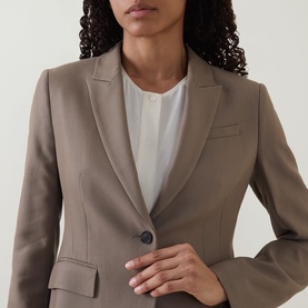 Model wearing a taupe single-button blazer with notch lapels, styled over a white top