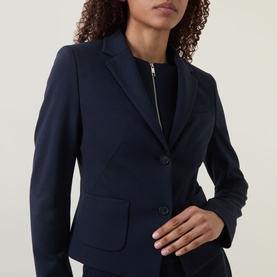 Model wearing a navy tailored blazer with notch lapels and two-button front, styled with a navy zip-detail top