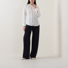 Model wearing Hugo Boss Optic White silk blouse with gathered neckline and long sleeves, styled with wide-leg black trousers.