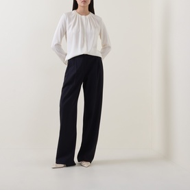 Model wearing Hugo Boss Optic White silk blouse with gathered neckline and long sleeves, styled with wide-leg navy trousers and cream heels.