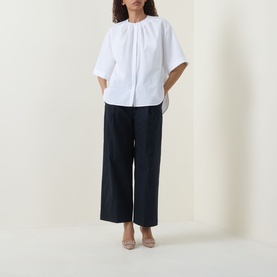 Model wearing Hugo Boss white cotton blouse with gathered neckline and wide sleeves, styled with navy wide-leg trousers and nude heels.
