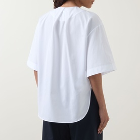 Model wearing Hugo Boss white cotton blouse, rear view, showing relaxed fit, curved hem and short sleeves, styled with navy trousers