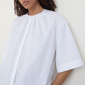 Model wearing Hugo Boss white cotton blouse with pleated neckline, concealed front placket and short wide sleeves, cropped view