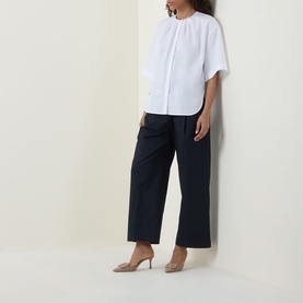 Model wearing Hugo Boss white cotton blouse with collarless neckline and short sleeves, styled with navy wide-leg trousers and nude heels
