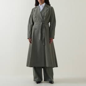 Model wearing sage green double-breasted belted maxi trench coat, styled with white shirt and wide-leg trousers