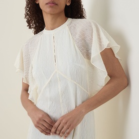 Model wearing Hugo Boss Optic Beige polyester dress with flutter sleeves, lace detail yoke, and pleated front panel.