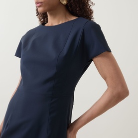 Model wearing Hugo Boss dark blue wool dress with cap sleeves, bateau neckline and fitted silhouette, paired with gold drop earrings.