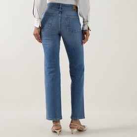 Model wearing Hugo Boss medium blue straight-leg jeans, rear view, styled with a white blouse and nude heeled mules.