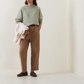 Model wearing Hugo Boss Fewena Brushed Sweater in Open Green with tan wide-leg trousers and brown loafers, carrying a cream jacket.